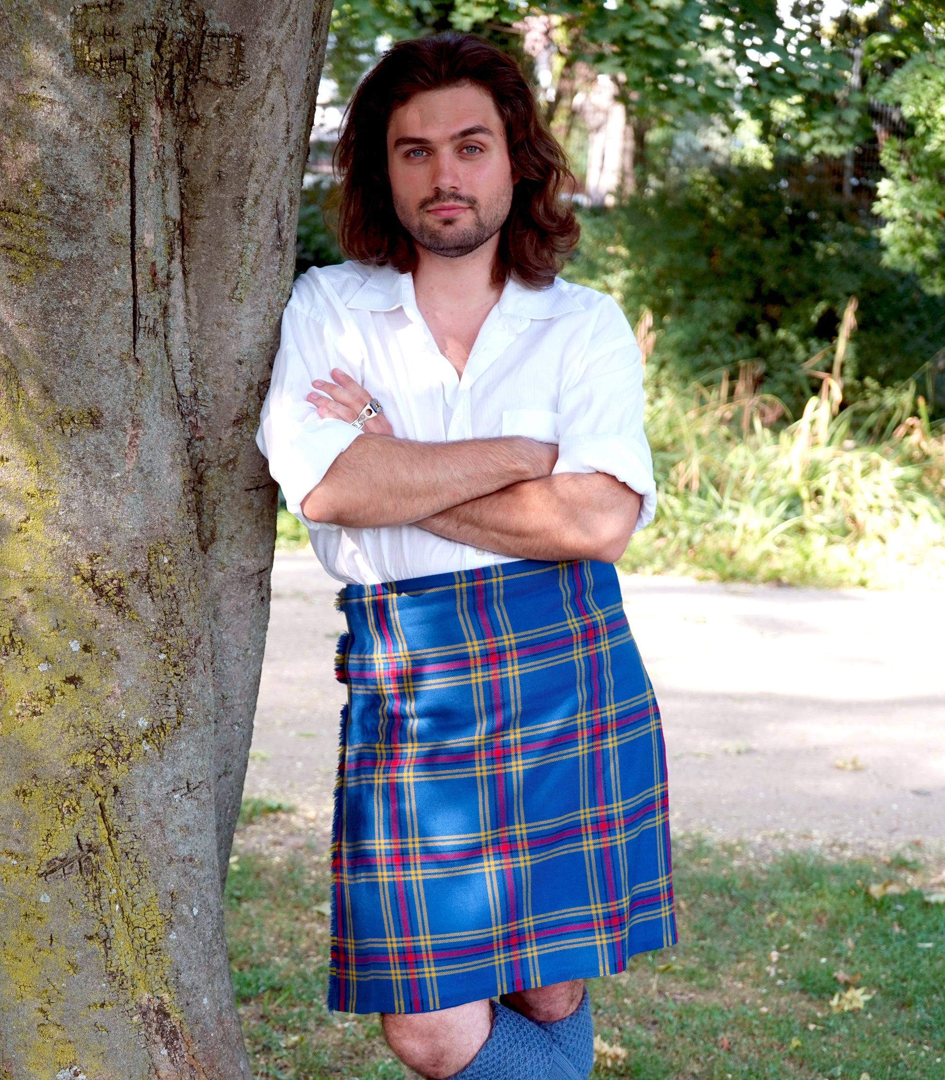 Person wearing a handmade European tartan kilt leaning against a tree