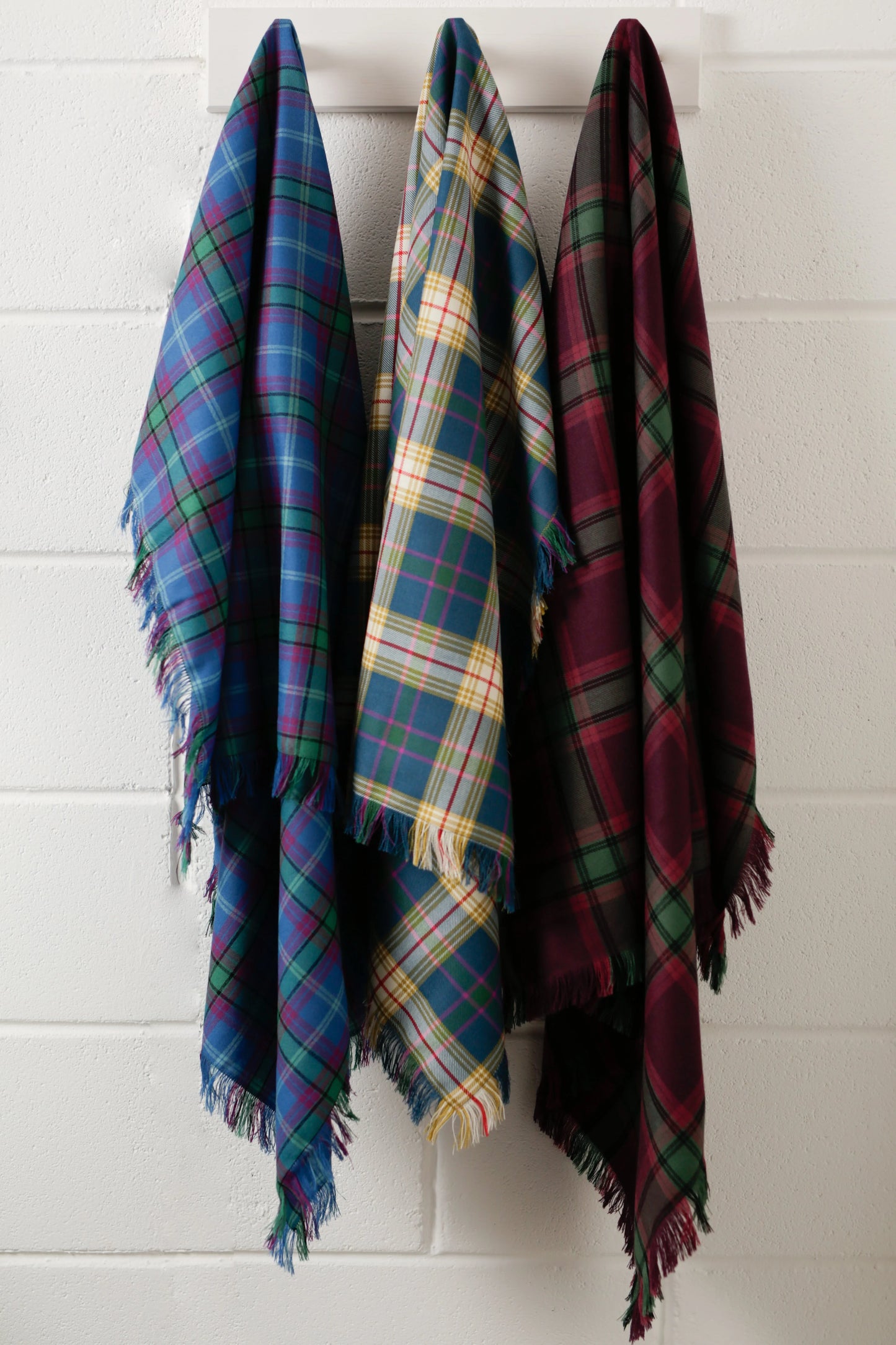 Three handmade tartan shawls draped hanging on pegs